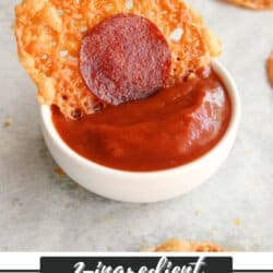 A crispy, round pepperoni chip is dipped into a small white bowl of reddish-brown sauce, with more chips in the background. Text reads: 2-ingredient Pepperoni Chips homemadeheather.com.