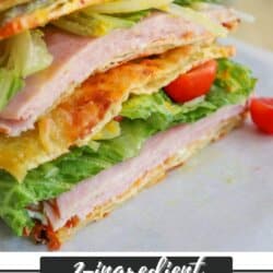 A sandwich made with layers of lettuce, ham, tomato, and a golden, thin, flatbread labeled as 2-ingredient pickle bread, is stacked and sliced on a white surface. Text at the bottom reads 2-ingredient pickle bread homemadetheather.com.