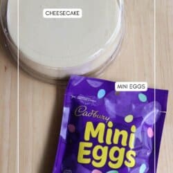 A round cheesecake in a pan is on a wooden surface. Next to it is a purple bag of Cadbury Mini Eggs. The bag is slightly open, showing the candy inside. The words CHEESECAKE and MINI EGGS are labeled on the image.