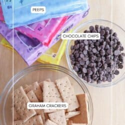 Bags of colorful Peeps marshmallows stacked on a table next to clear bowls containing chocolate chips and graham crackers. Labels are placed above each item, naming them.