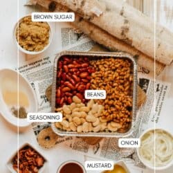 Top-down view of ingredients for baked beans arranged on a table, including a pan of mixed beans, bowls of brown sugar, sliced onion, bacon, seasoning, mustard, and barbecue sauce, on a newspaper background.