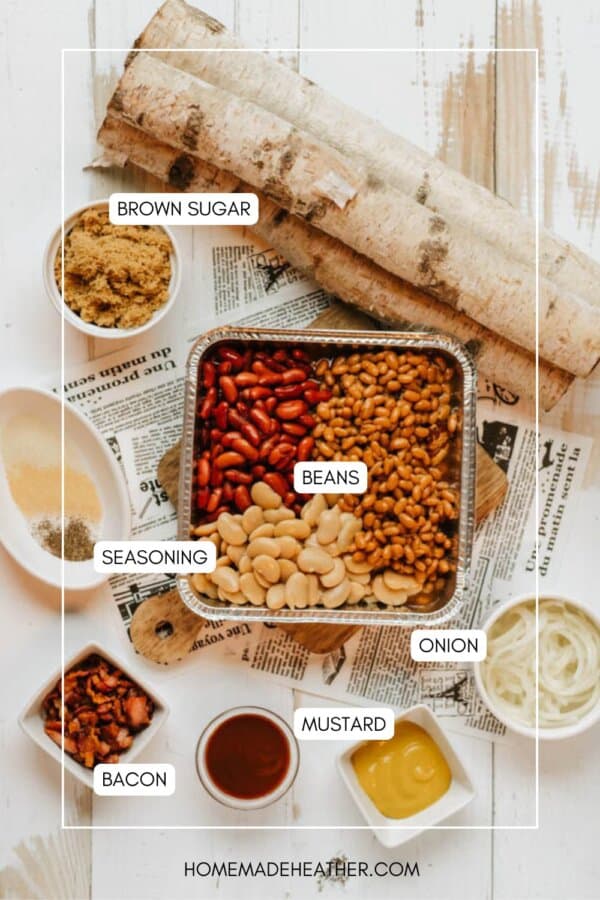 Top-down view of ingredients for baked beans arranged on a table, including a pan of mixed beans, bowls of brown sugar, sliced onion, bacon, seasoning, mustard, and barbecue sauce, on a newspaper background.