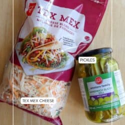A bag of Tex Mex shredded cheese and a jar of sandwich sliced pickles sit on a light wooden surface. Each item is labeled: โTEX MEX CHEESEโ and โPICKLESโ.
