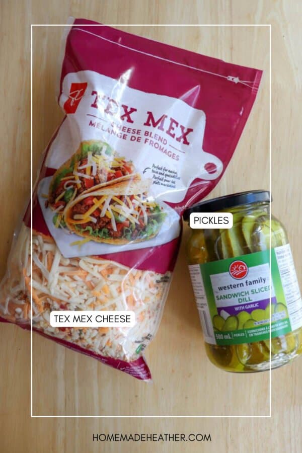 A bag of Tex Mex shredded cheese and a jar of sandwich sliced pickles sit on a light wooden surface. Each item is labeled: โTEX MEX CHEESEโ and โPICKLESโ.