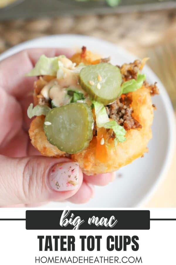 Close-up of a hand holding a tater tot cup filled with ground beef, lettuce, pickles, cheese, and sauce, resembling a Big Mac. Text at the bottom reads big mac tater tot cups and homemadeheather.com.