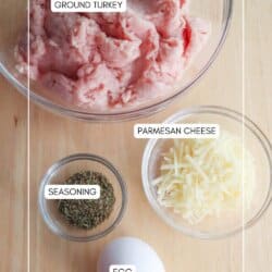 Top-down view of a wooden surface with ingredients for a recipe: a bowl of ground turkey, a small bowl of parmesan cheese, a smaller bowl of herbs for seasoning, and a whole egg.