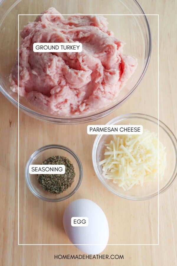 Top-down view of a wooden surface with ingredients for a recipe: a bowl of ground turkey, a small bowl of parmesan cheese, a smaller bowl of herbs for seasoning, and a whole egg.