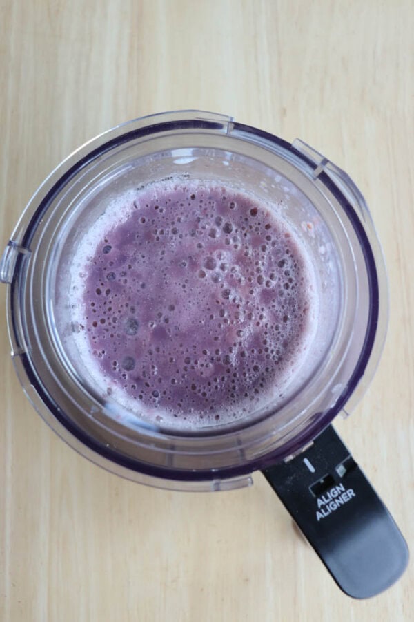 Top view of a blender filled with a frothy purple smoothie on a light wooden surface. The lid is transparent with a dark handle that has the words ALIGN ALIGNER printed on it.