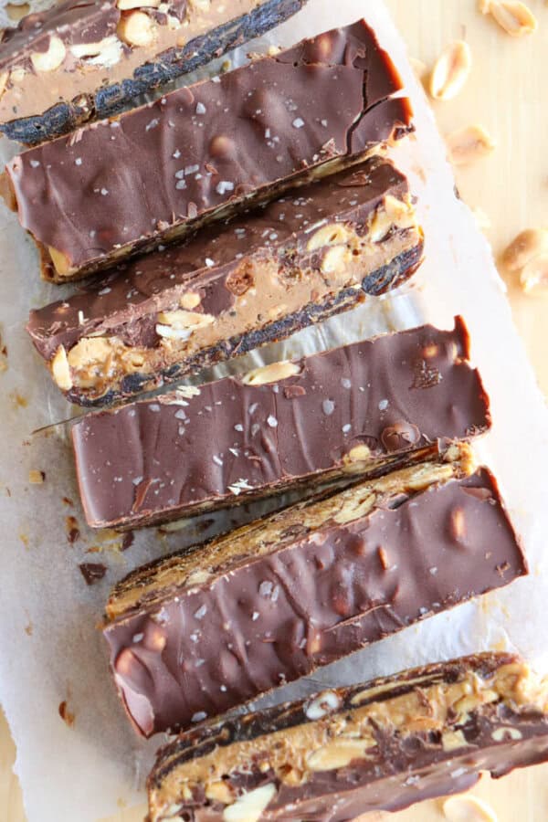 Five chocolate-covered snack bars filled with nuts, cut into slices and arranged on parchment paper. The surface is slightly textured, and there are a few scattered nuts around.