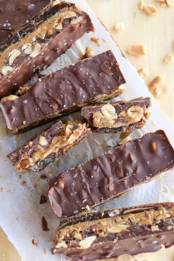 Close-up of chocolate bars filled with peanuts and nougat, arranged on parchment paper. The bars are sliced to show the layers of chocolate, peanuts, and nougat, with a few scattered peanuts around them.