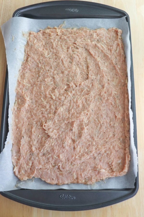 Ground meat mixture spread evenly on a parchment-lined baking sheet, ready for cooking.