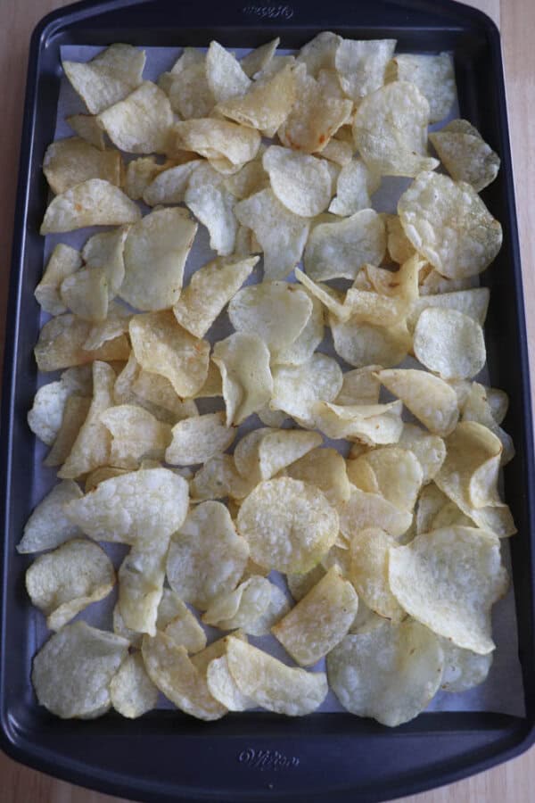 A baking tray filled with a single layer of golden potato chips on a wooden surface.