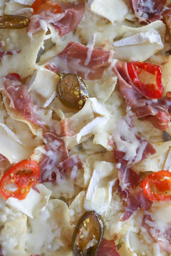 Close-up of nachos topped with melted cheese, slices of cured meat, and rings of red and green peppers. The crispy chips are layered with various toppings, creating a colorful and appetizing dish.