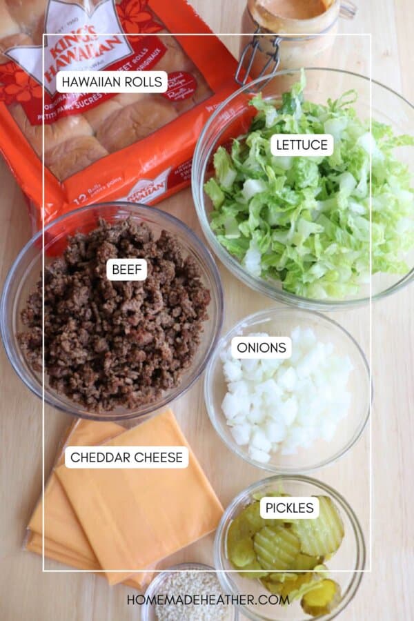 A top-down view of ingredients for sliders: a package of Hawaiian rolls, a bowl of shredded lettuce, cooked ground beef, diced onions, sliced cheddar cheese, and chopped pickles, all arranged on a table.