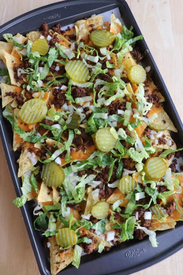 A tray of nachos topped with ground beef, melted cheese, shredded lettuce, chopped onions, and sliced pickles.