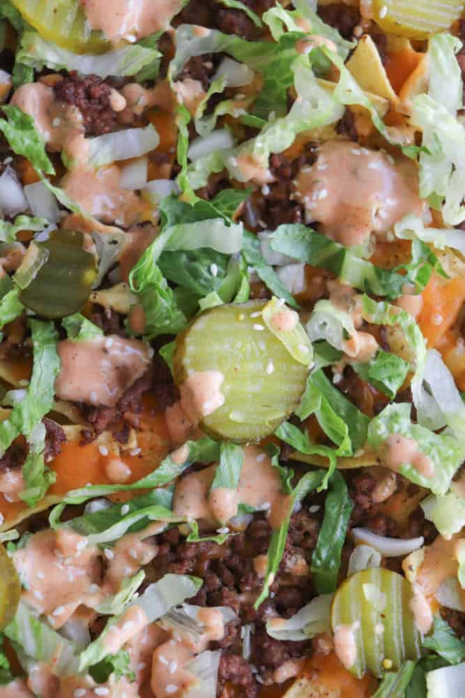 Close-up of a cheeseburger-inspired dish topped with ground beef, shredded lettuce, pickles, diced onions, shredded cheese, and drizzled with creamy sauce.