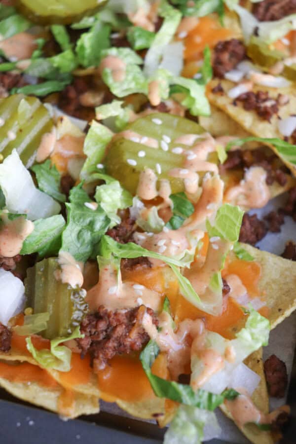 Close-up of nachos topped with ground beef, melted cheddar cheese, lettuce, diced onions, pickles, and a drizzle of creamy sauce.