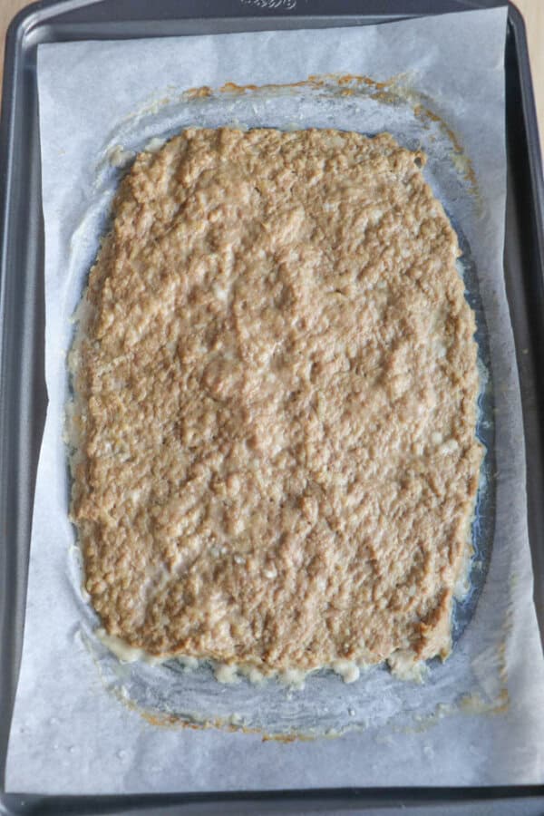 A rectangular, uncooked dough mixture is spread on a parchment-lined baking sheet, ready to be baked. The dough has a coarse texture and uneven edges.