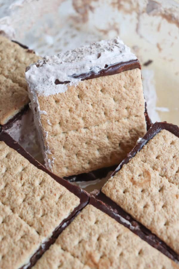 Close-up of homemade smores treats with graham cracker squares sandwiching layers of chocolate and gooey marshmallow, stacked together in a dish.