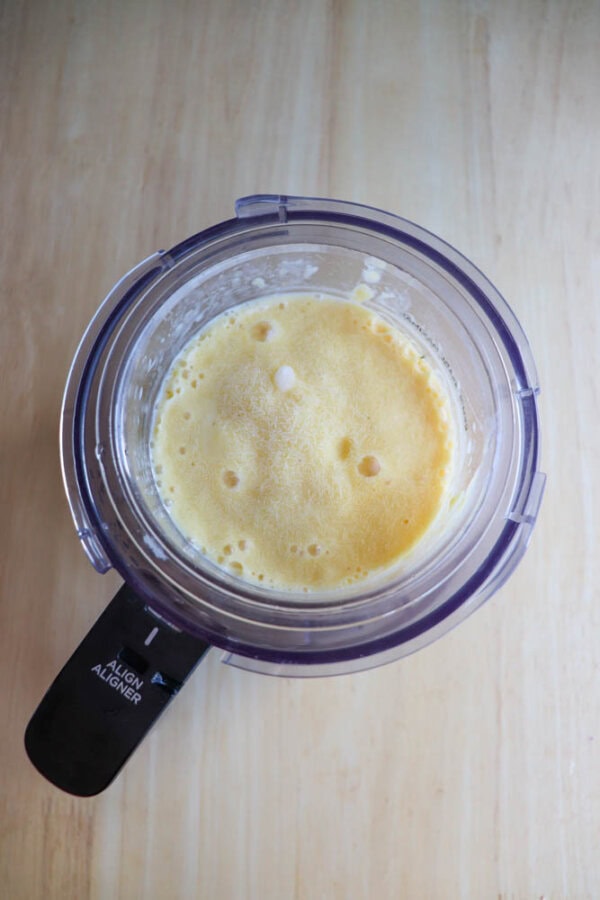 Top-down view of a blender with a creamy yellow mixture inside, sitting on a light wooden surface.