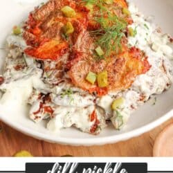 A bowl of smashed potato salad topped with crispy potato slices, chopped pickles, fresh dill, and creamy dressing, served on a white plate with a lemon slice and a fork nearby. Text reads: Dill Pickle Smashed Potato Salad.