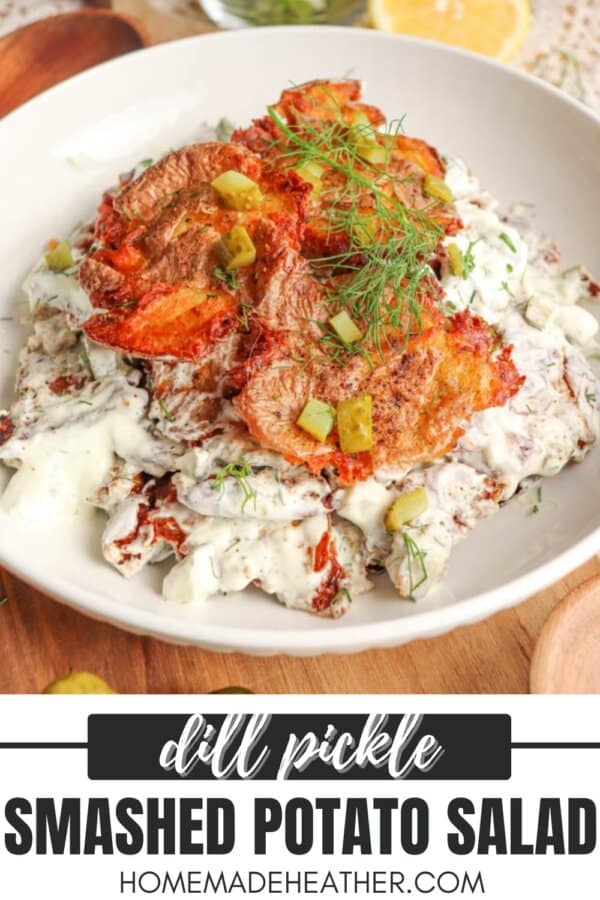 A bowl of smashed potato salad topped with crispy potato slices, chopped pickles, fresh dill, and creamy dressing, served on a white plate with a lemon slice and a fork nearby. Text reads: Dill Pickle Smashed Potato Salad.