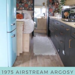 Interior of a restored 1975 Argosy Airstream featuring a light blue retro fridge, dark cabinets, a cozy bed with pillows, floral wallpaper, and wood flooring. Text overlay reads, Argosy Airstream restoration.