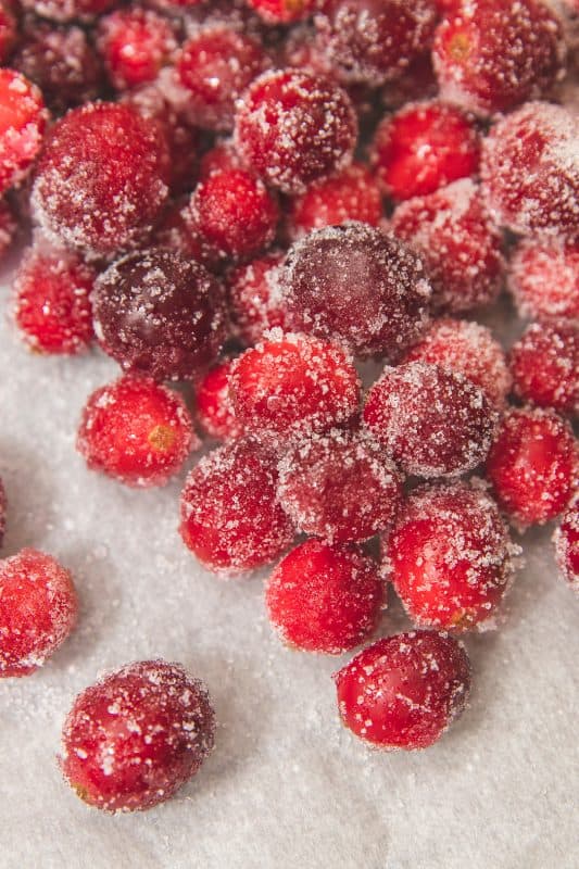 Close-up of sugared cranberries scattered on a light surface, coated with a layer of granulated sugar, creating a sparkling, frosted appearance.