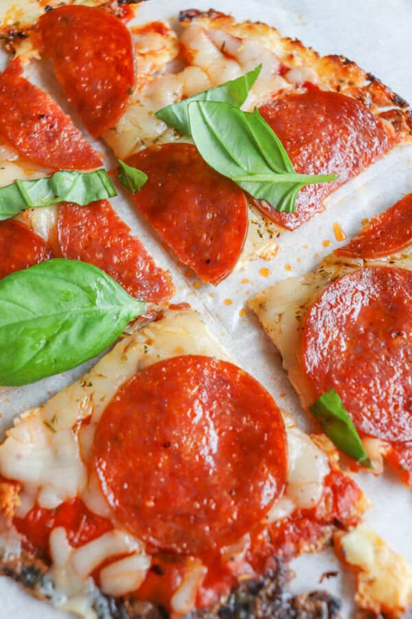 Close-up of sliced pepperoni pizza topped with fresh basil leaves, melted cheese, and tomato sauce, on a parchment-lined surface.