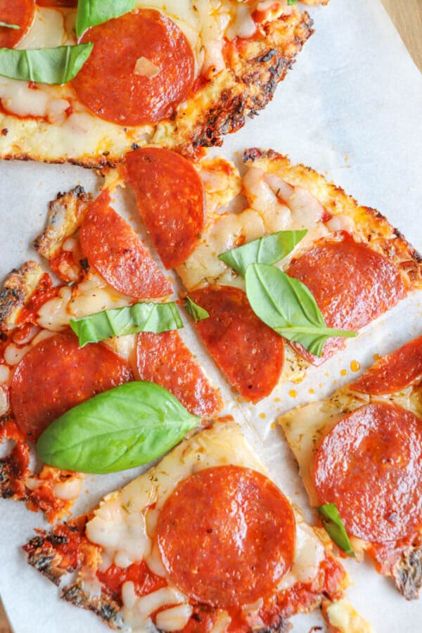 Close-up of sliced pepperoni pizza with melted cheese and fresh basil leaves on top, served on parchment paper.