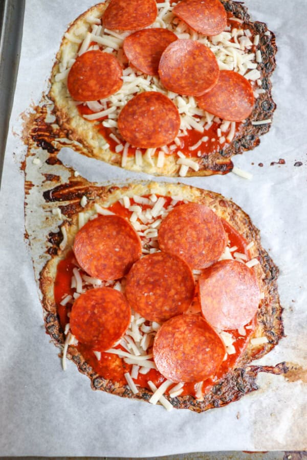Two irregularly shaped homemade pizzas on parchment paper, topped with tomato sauce, shredded cheese, and pepperoni slices. The crust edges appear slightly crispy and browned.