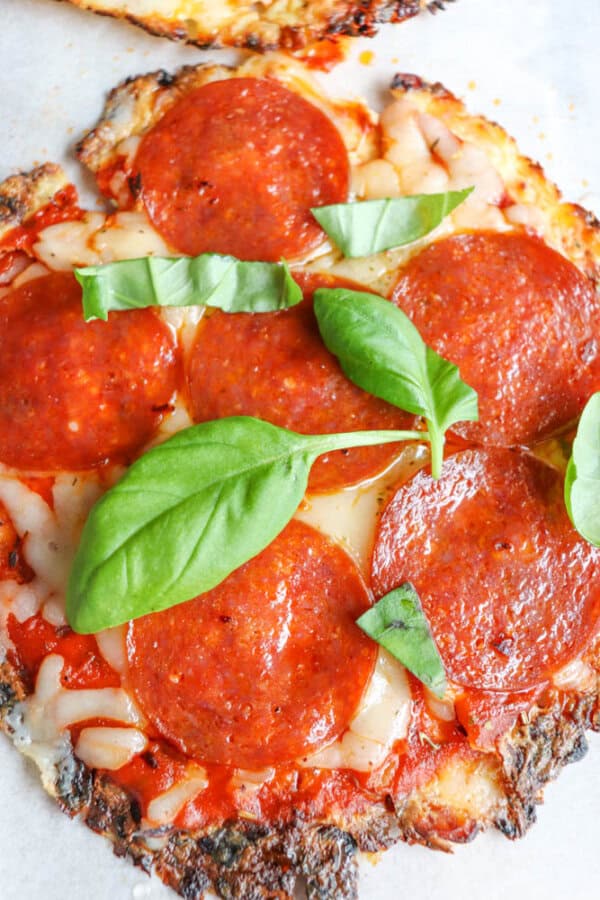 Close-up of a pepperoni pizza topped with melted cheese, tomato sauce, and fresh basil leaves on a slightly crispy crust.