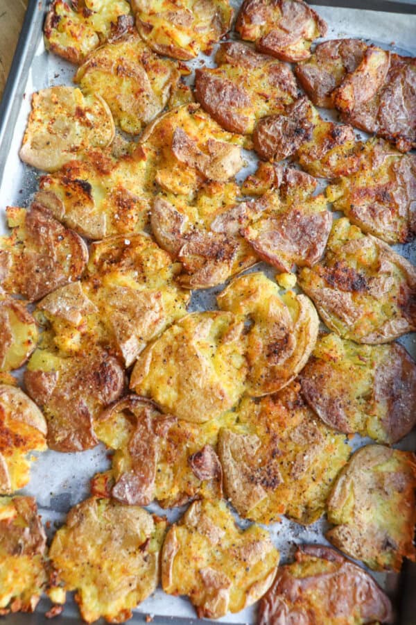 A baking sheet covered with crispy, golden-brown smashed potatoes, seasoned and baked, resting on parchment paper.