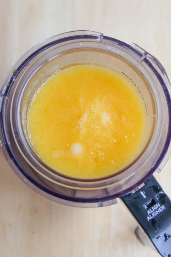 Overhead view of a blender container filled with a yellow, frothy liquid mixture for ninja creami peach sorbet, sitting on a light wooden surface.