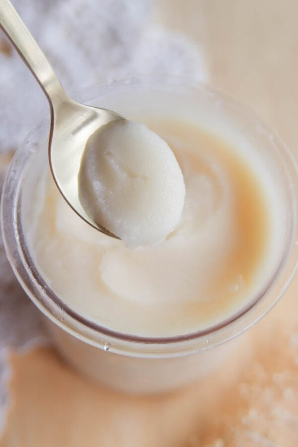 A close-up of a spoon scooping creamy, white coconut butter from a small glass jar, with a light-colored background and a textured cloth partially visibleโperfect for pairing with your favorite Ninja Creami pear sorbet recipe.