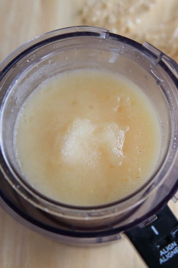 A close-up of a food processor bowl filled with a smooth, light yellow mixture, likely from a Ninja Creami pear sorbet recipe, sitting on a wooden surface.