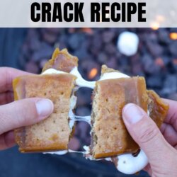 Two hands pull apart a gooey smores crack recipe dessert bar, oozing caramel and melted marshmallow, with a fire pit in the background. Text on the image reads Smores Crack Recipe and homemadeheather.com.