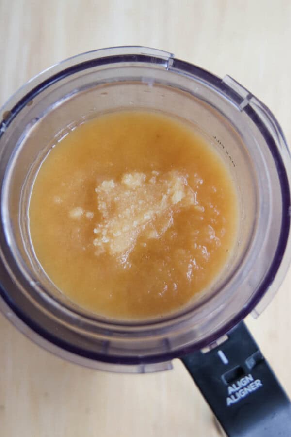 A top view of a blender containing a light orange, semi-liquid mixture with grated cheese on top, set on a light wooden surface.