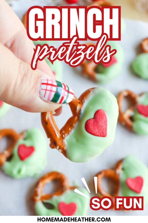 A hand holding a pretzel dipped in green coating with a red heart sprinkle, surrounded by more pretzels on a tray. Text reads: Grinch pretzels, SO FUN, homemadeheather.com.