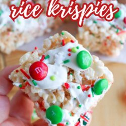 A hand holds a Christmas-themed Rice Krispies treat topped with white icing, red and green M&Ms, and festive sprinkles. More decorated treats are blurred in the background. Text reads: Christmas rice krispies. So easy!.