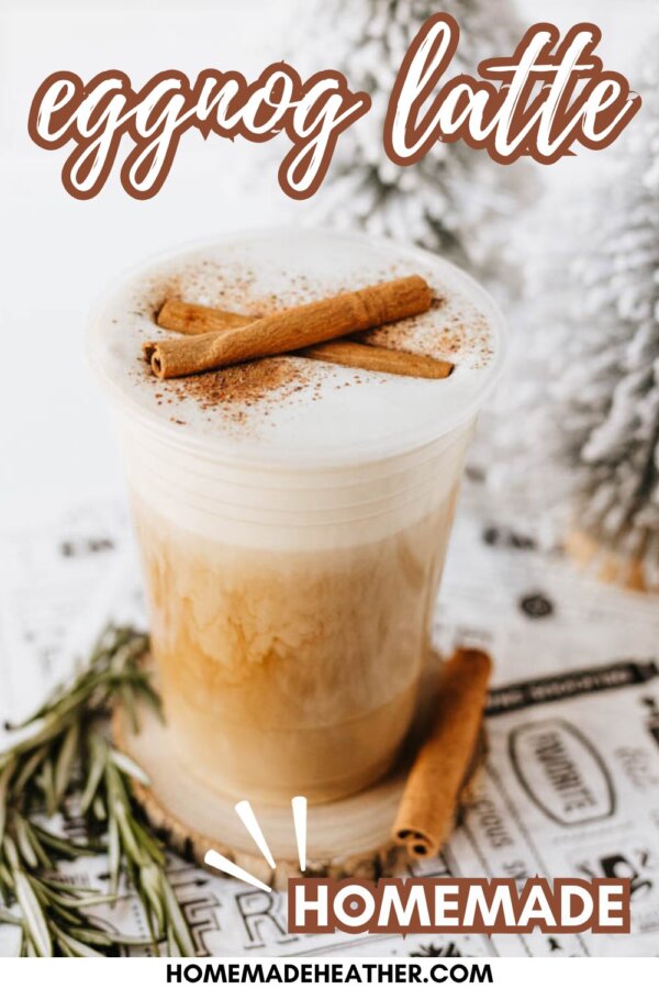 A creamy eggnog latte topped with cinnamon sticks and sprinkled with cinnamon sits on a table with rosemary sprigs, holiday decorations, and text reading eggnog latte and homemade above and below the drink.