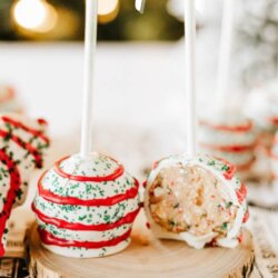 Three festive cake pops with red and green drizzle sit on a wooden slice. One is bitten to show the inside. Text reads: “Little Debbie cake pops” and “homemadeheather.com.”.