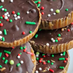 A stack of chocolate-covered Ritz crackers topped with red, green, and white sprinkles sits on a white plate. The text reads Ritz Christmas crack cookies and homemadeheather.com.