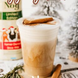 A frothy eggnog latte in a clear cup garnished with a cinnamon stick sits on a holiday-themed surface. A carton of eggnog and festive decor, including pine sprigs, appear in the background. Text: “eggnog latte” and “homemadeheather.com”.