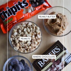 Five baking ingredients on a wooden surface: a bag of peanut butter chips, a bowl of peanut butter, a bowl of peanuts, a bar of Bakerโs chocolate, and a bowl of melting chocolate, each labeled with text.