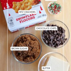 A box of Ritz crackers, bowls of brown sugar, chocolate chips, and sprinkles, plus a dish of butter are arranged on a wooden surface, labeled with their names.