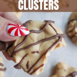 A hand with festive red and white striped nail art holds a peanut butter cluster drizzled with chocolate. More clusters are on a light surface. Text reads: โCrockpot Peanut Butter Clusters HomemadeHeather.com.โ.