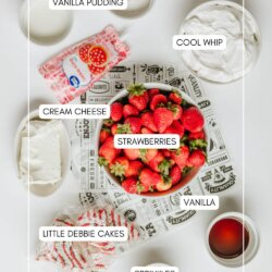 A flat lay of ingredients for a dessert: a bowl of strawberries, vanilla pudding, cool whip, cream cheese, vanilla, Little Debbie cakes, and containers of red and green sprinkles are all labeled and arranged on a white surface.
