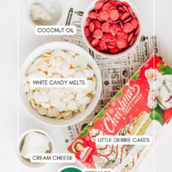 A flat lay of baking ingredients: bowls of white and red candy melts, coconut oil, cream cheese, green sprinkles, and a box of Little Debbie Christmas Tree Cakes on vintage papers—each item is labeled.