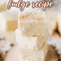 A close-up of creamy eggnog fudge squares stacked on a small wooden platter, topped with a sprinkle of spice. Text overlay reads: Eggnog fudge recipe SO EASY. Website homemadeheather.com is at the bottom.